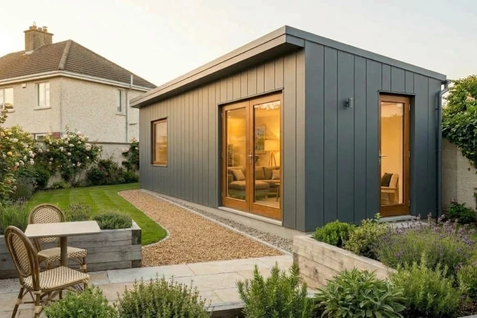 A finished modular garden home in anthracite panels with a mono-pitch roof, a window and glazed double doors, beside a patio and planters