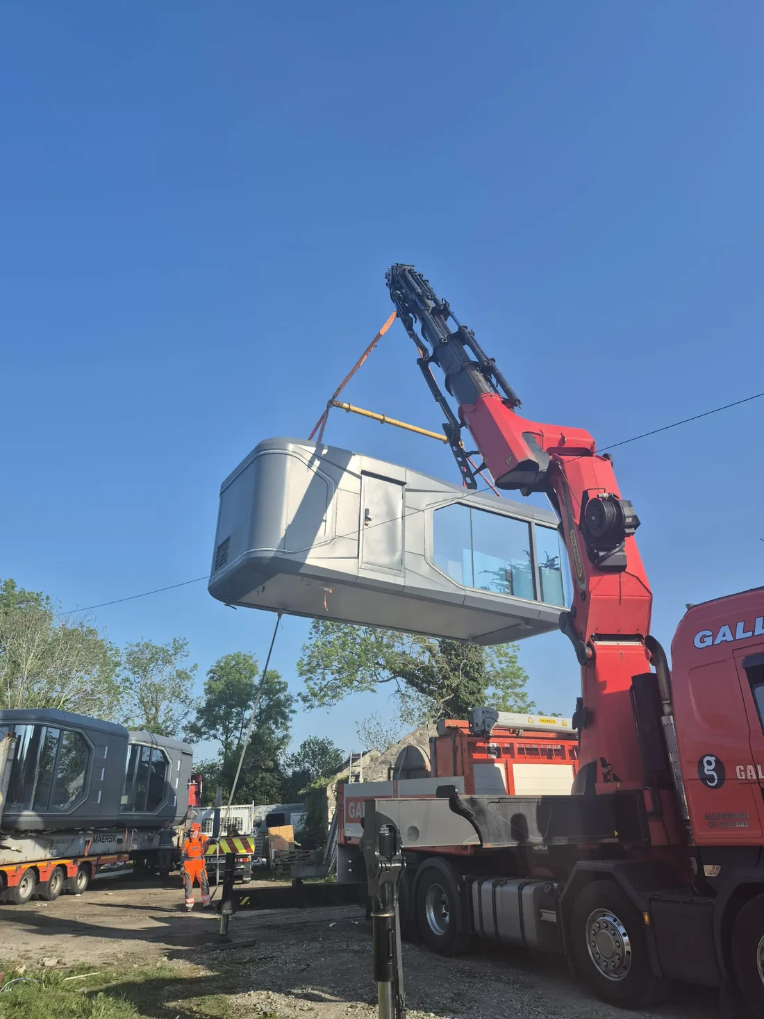 A pod being lifted off a lorry by a truck-mounted crane, with a second pod waiting on a trailer
