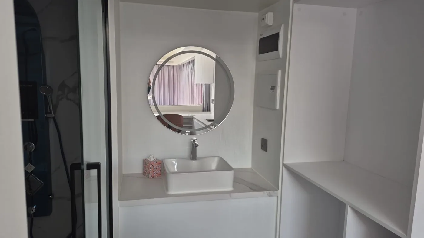 A washbasin under a round lit mirror in a pod bathroom