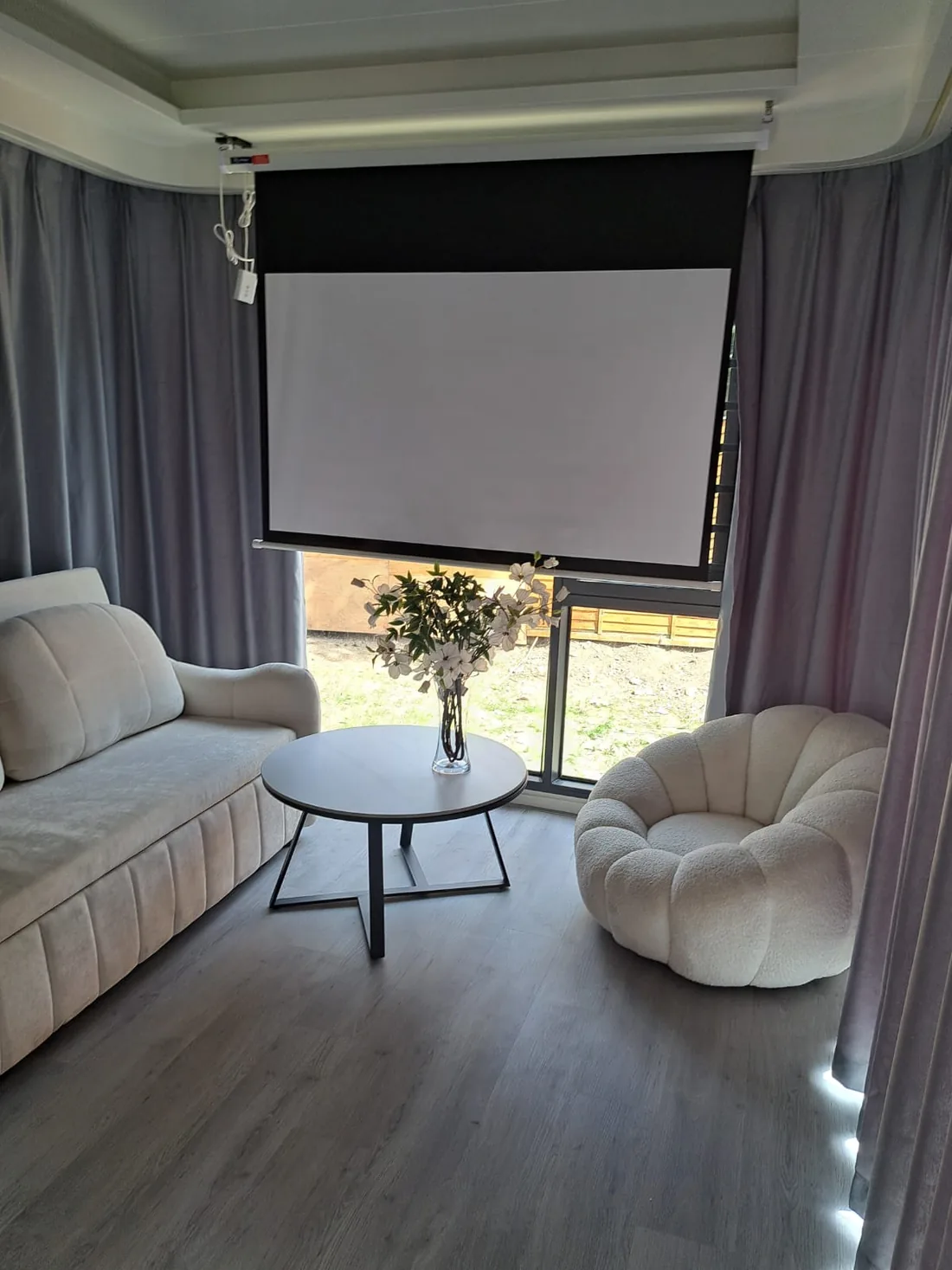 Pod living area with a cream sofa, round table and a drop-down screen